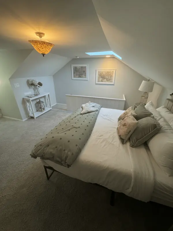 Bright attic bedroom with a made bed, skylight and decorated console