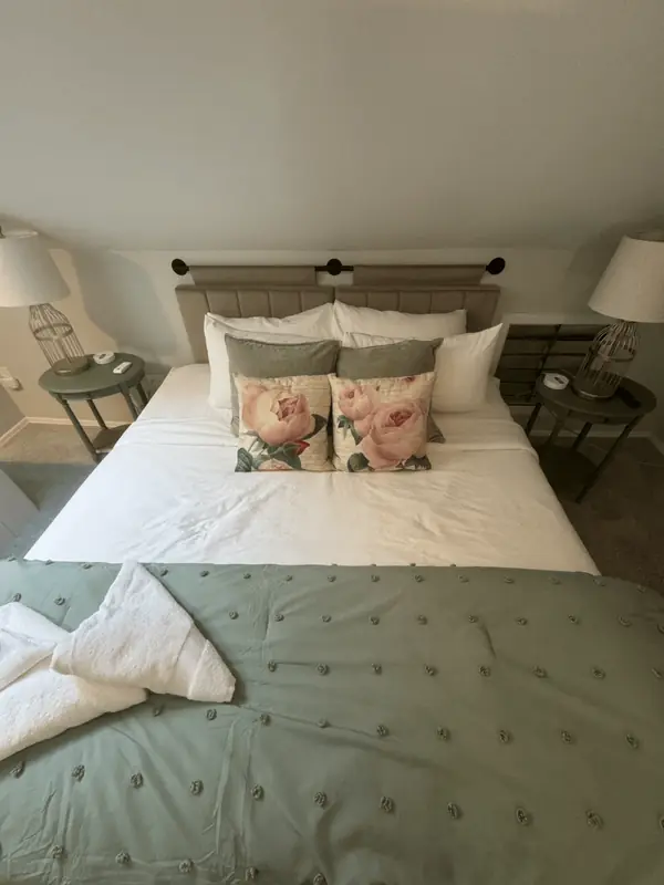 Made bed with rose pillows and a green tufted throw