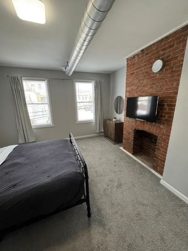 Clean bedroom with a brick fireplace, wall TV and fresh carpet