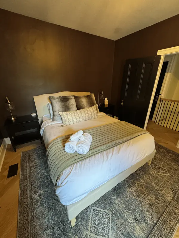Bedroom with dark walls, a made bed and rolled towels on a quilted throw