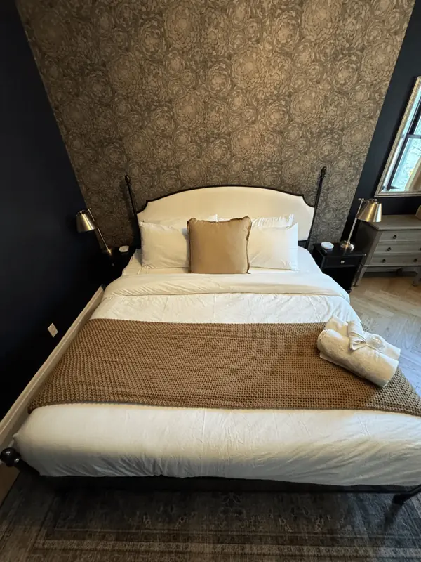 Bed with crisp white bedding and a knit throw against a floral wallpaper wall